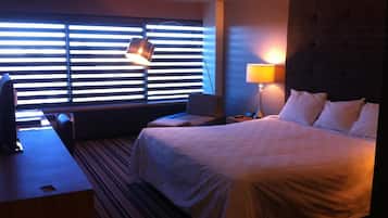 Una habitación de hotel con cama, escritorio, silla, lámpara y televisión.