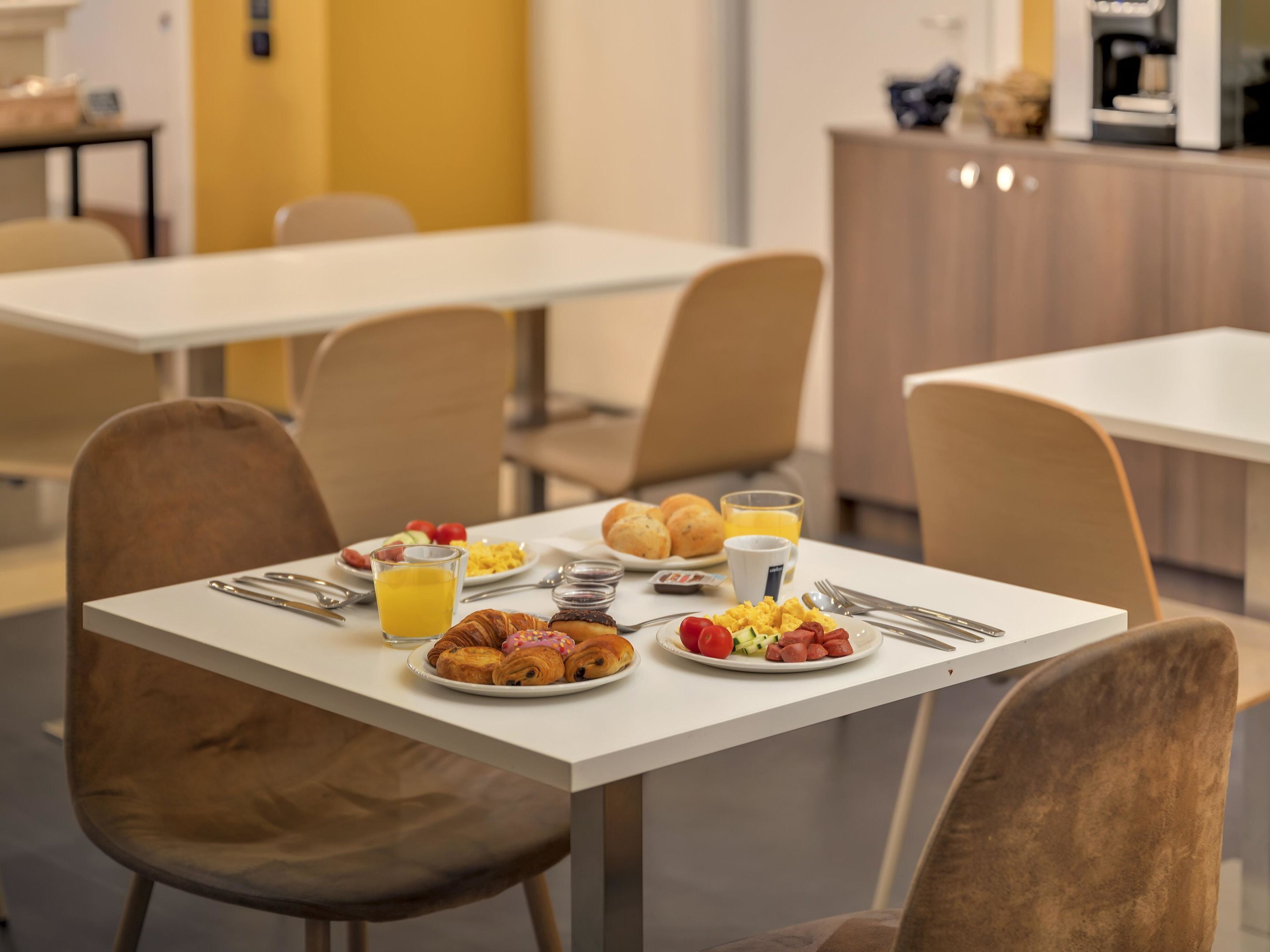A breakfast setting with a table set for two, including croissants, scrambled eggs, tomatoes, and orange juice.