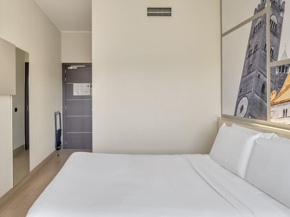 Habitación de hotel con una cama grande, un armario, un espejo y un cuadro con una torre.