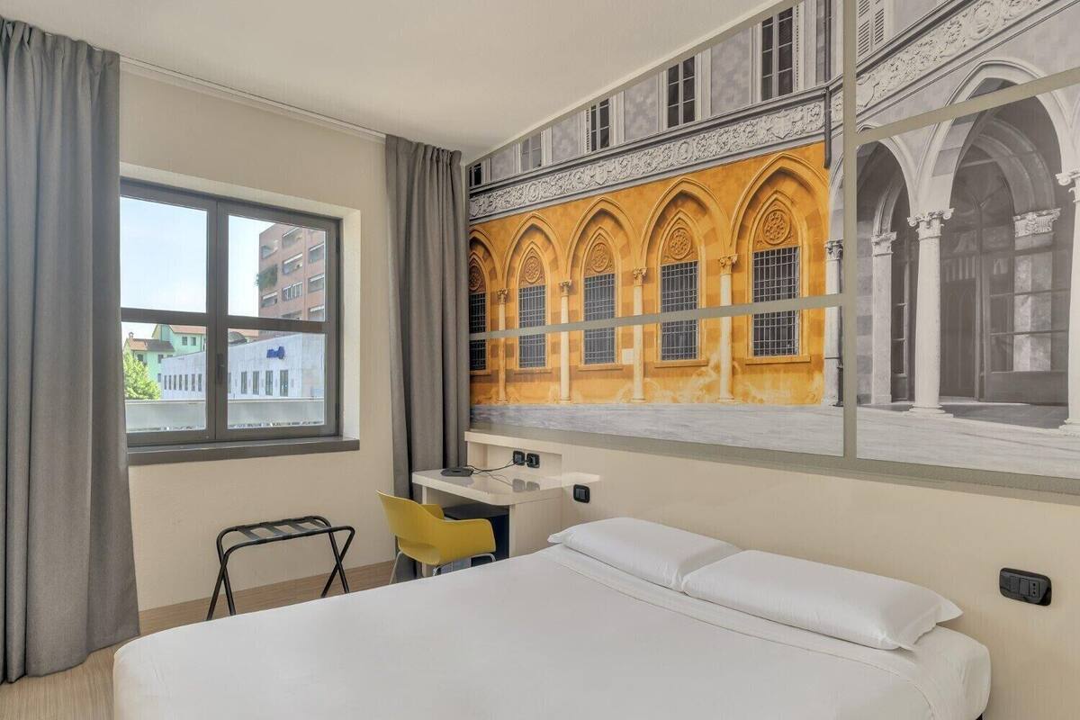 A hotel room with a bed, a desk, a chair, and a large window.