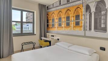 A hotel room with a bed, a desk, a chair, and a large window.