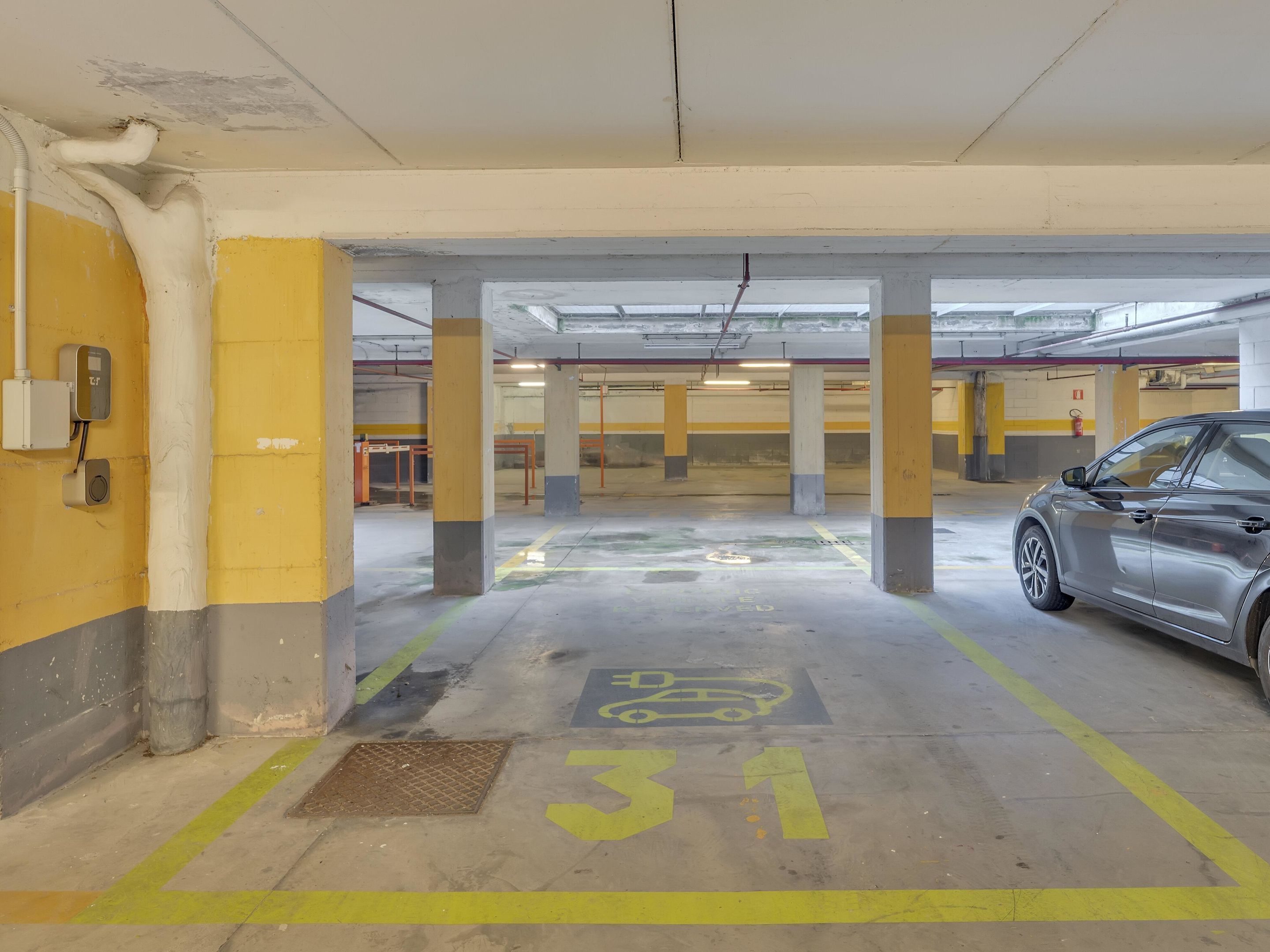 A parking garage with yellow and grey pillars, a car parked in a designated spot, and a security camera on the wall.