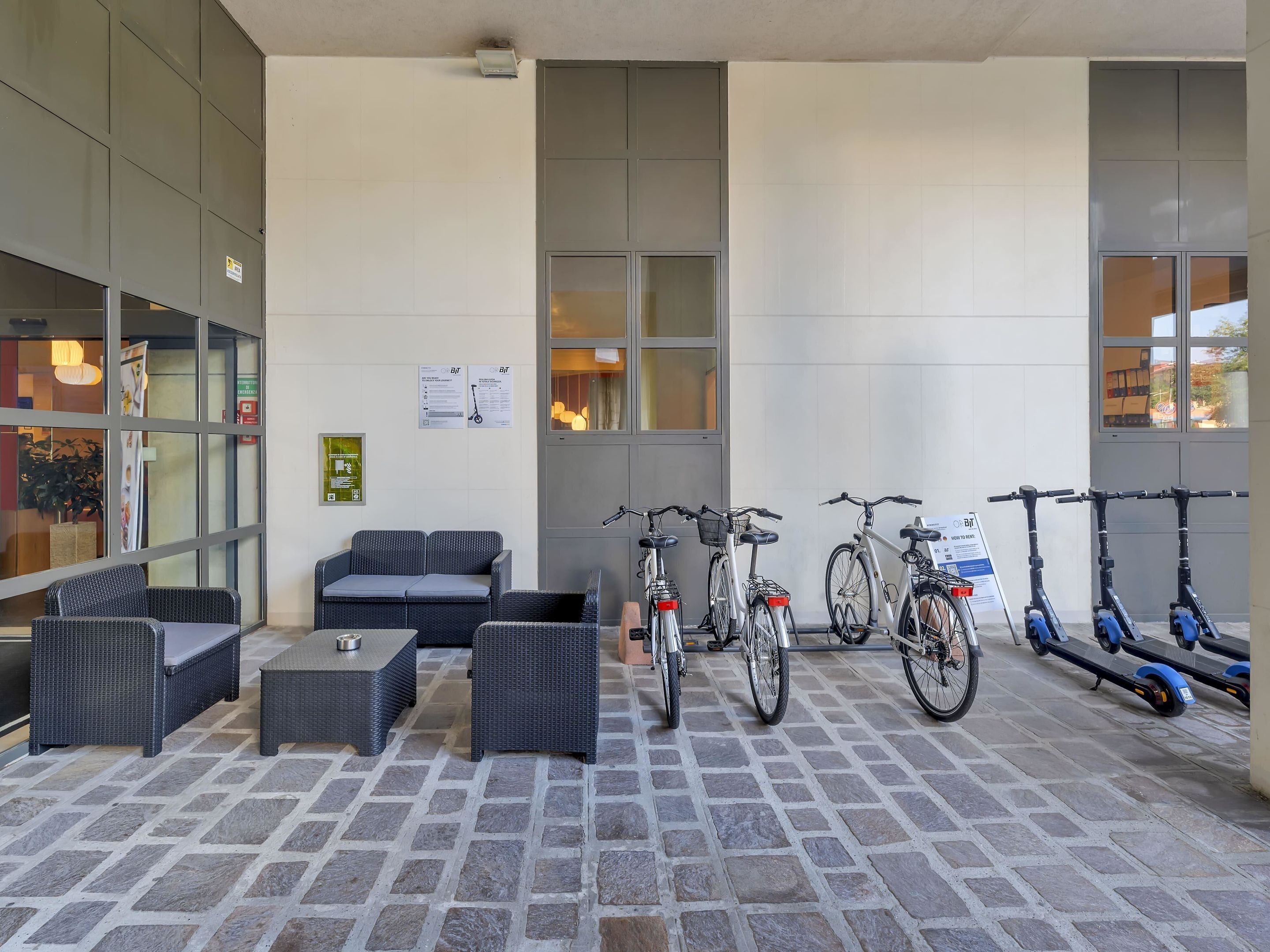 A covered outdoor seating area with wicker furniture, bicycles, and scooters.