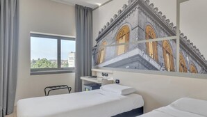 Une chambre d’hôtel avec deux lits, une fenêtre donnant sur un beau paysage, un bureau avec un ordinateur et une fresque murale.