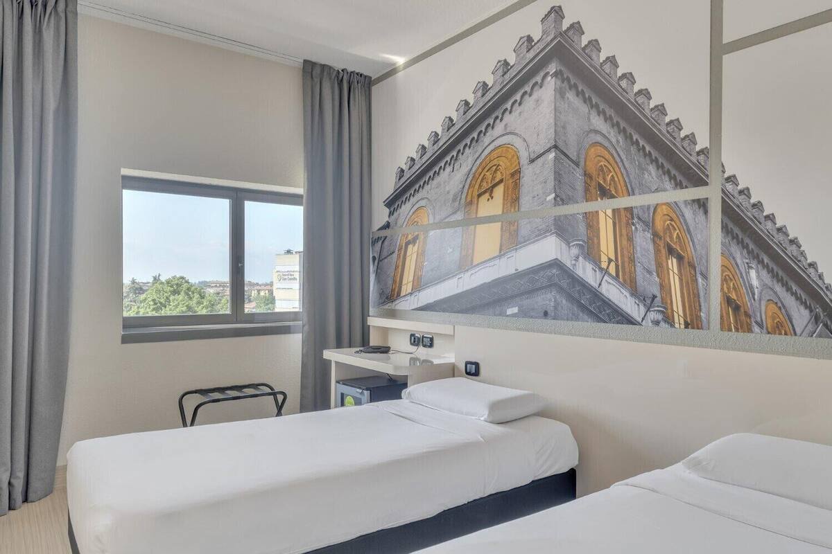 A hotel room with two beds, a window with a view, a desk with a computer, and a wall mural.