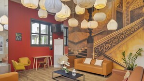 Un hall d’hôtel moderne avec des canapés orange, une table basse et des lanternes en papier suspendues.