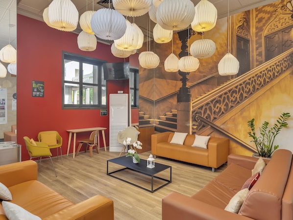 Un hall d’hôtel moderne avec des canapés orange, une table basse et des lanternes en papier suspendues.