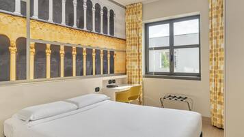 Une chambre d’hôtel comprenant un lit, un bureau, une chaise, une fenêtre et une vue sur un édifice architectural doté d’arcades.