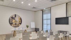 Une salle de conférence avec des chaises blanches, une table ronde avec des bouteilles d’eau, un tableau blanc et une grande fenêtre.