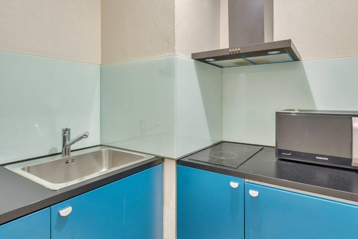 A compact kitchen with a stainless steel sink, a black induction cooktop, and blue cabinets.