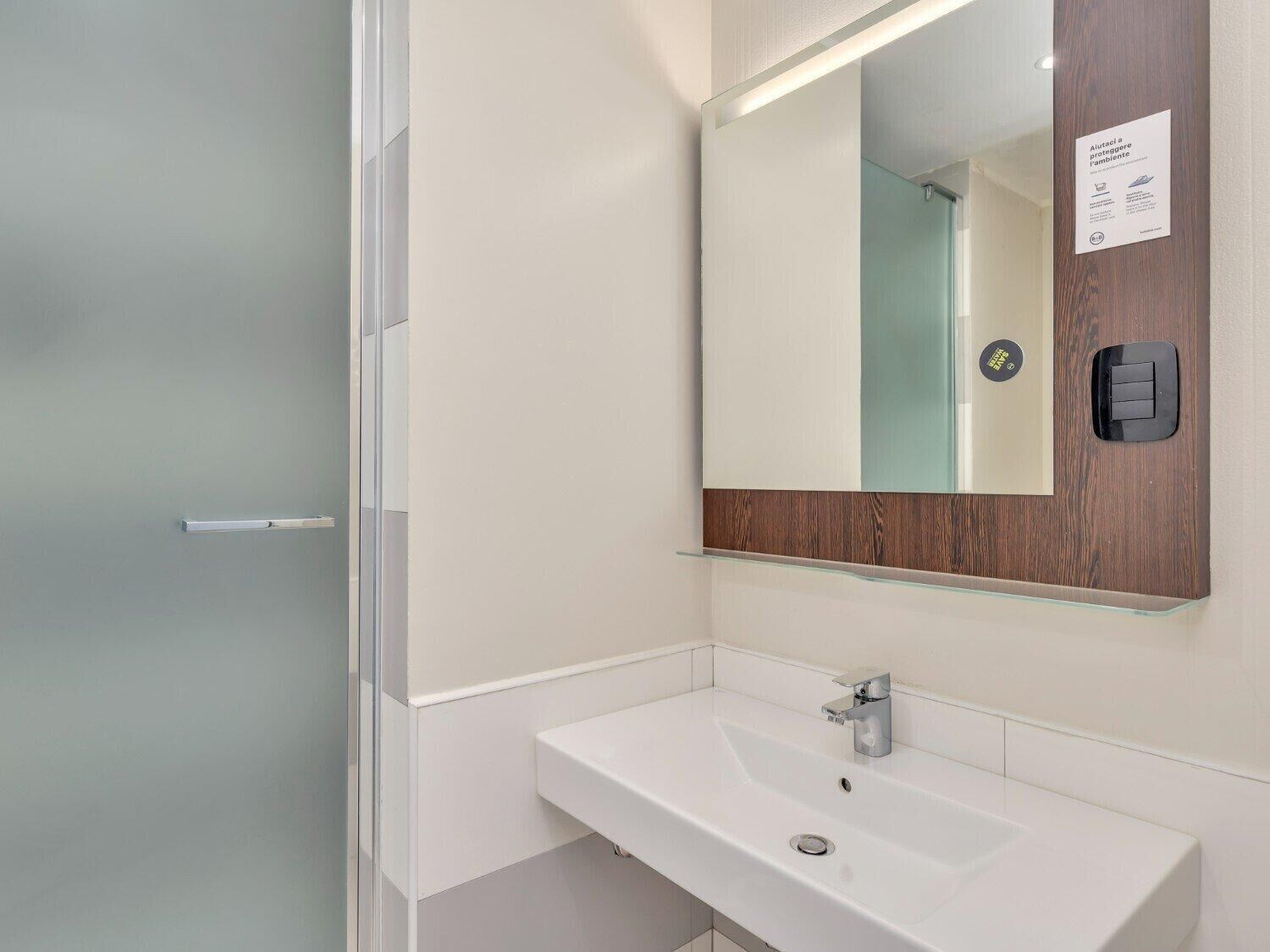 Une salle de bain moderne avec un lavabo blanc, un miroir avec un cadre en bois et une porte en verre dépoli.