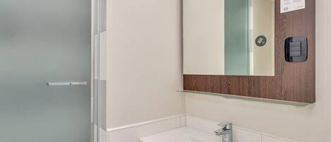 Un baño moderno con un lavabo blanco, un espejo con marco de madera y una puerta de vidrio esmerilado.