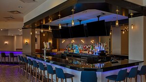 Zona de bar con una barra alargada, varios taburetes y una amplia selección de botellas.