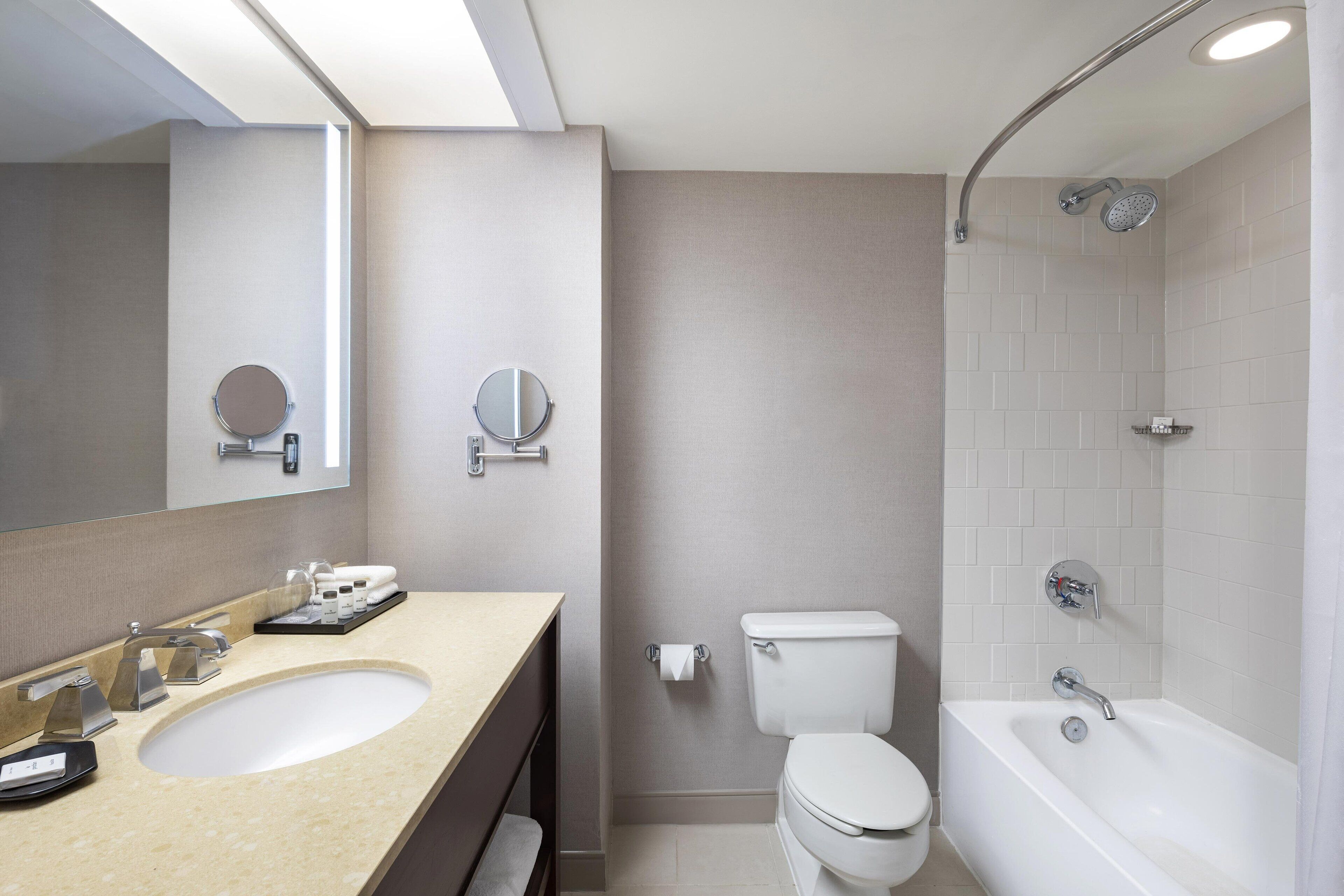 A modern bathroom with a sink, two mirrors, a toilet, and a bathtub.