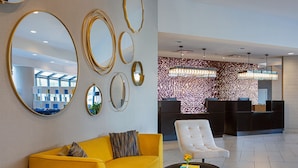 Un moderno vestíbulo de hotel con un sofá amarillo, un sillón blanco y una recepción con papel tapiz estampado.