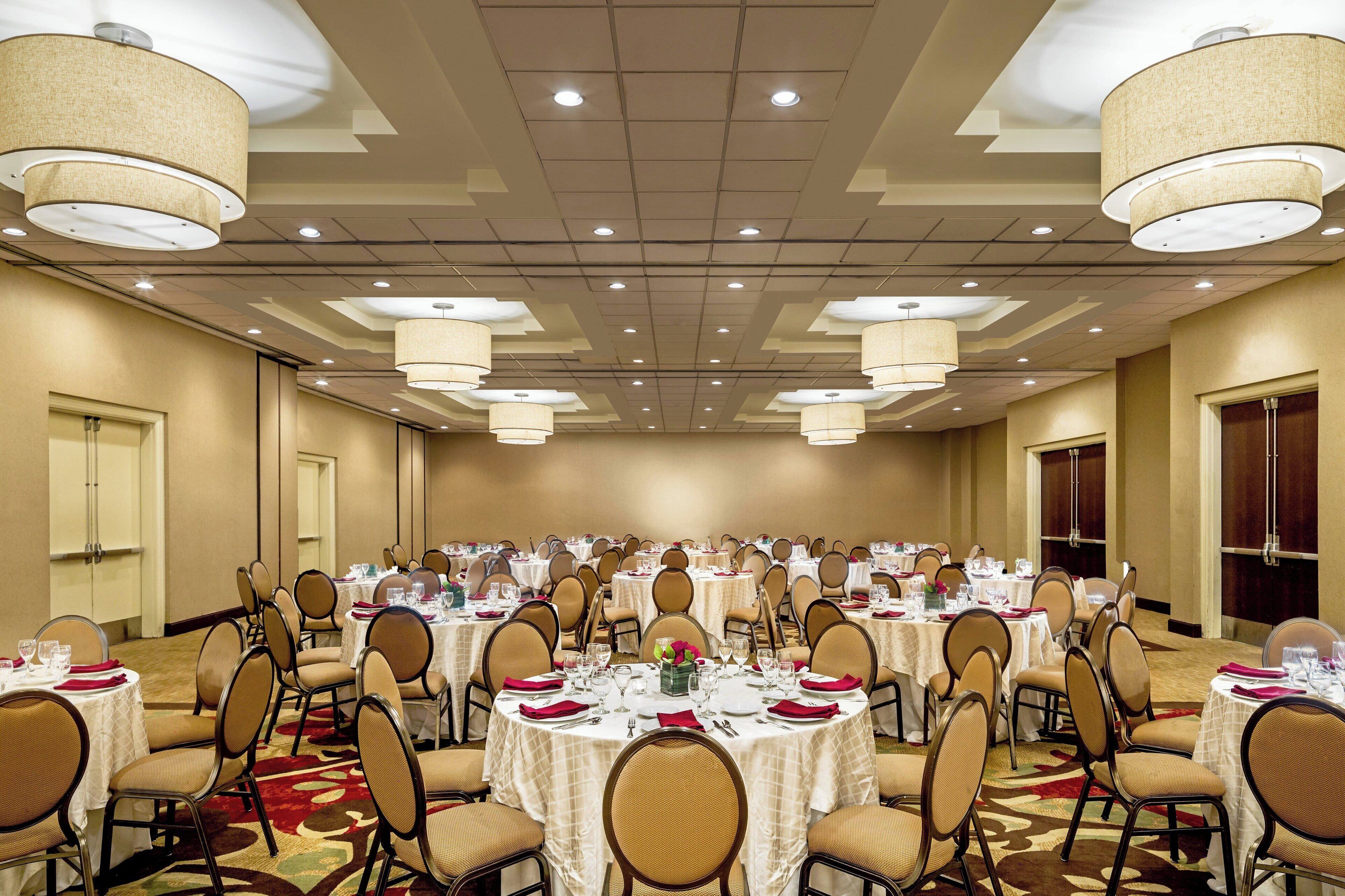 A large banquet hall with round tables, chairs, and chandeliers.