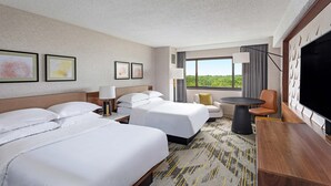 A hotel room with two beds, a desk, a chair, and a TV.