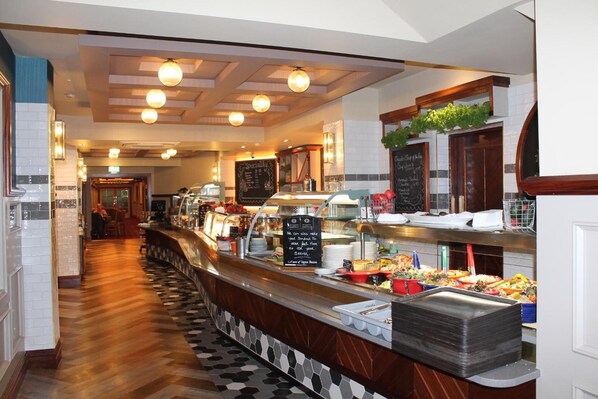 A buffet area with a variety of food items, a chalkboard menu, and a counter with stacked plates.