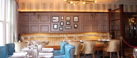 A formal dining area with a long table, blue and brown upholstered chairs, and a patterned floor.