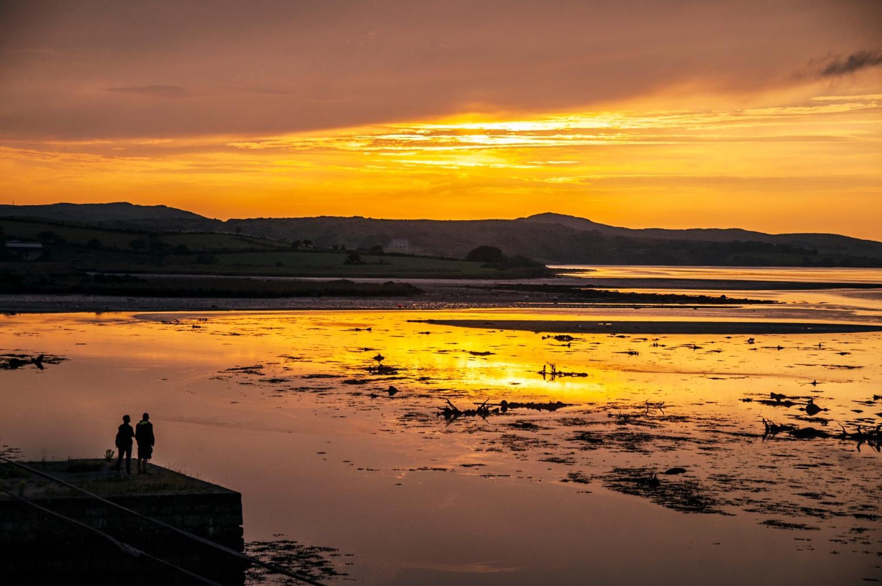 A sunset over a calm body of water with silhouettes of people on a dock.