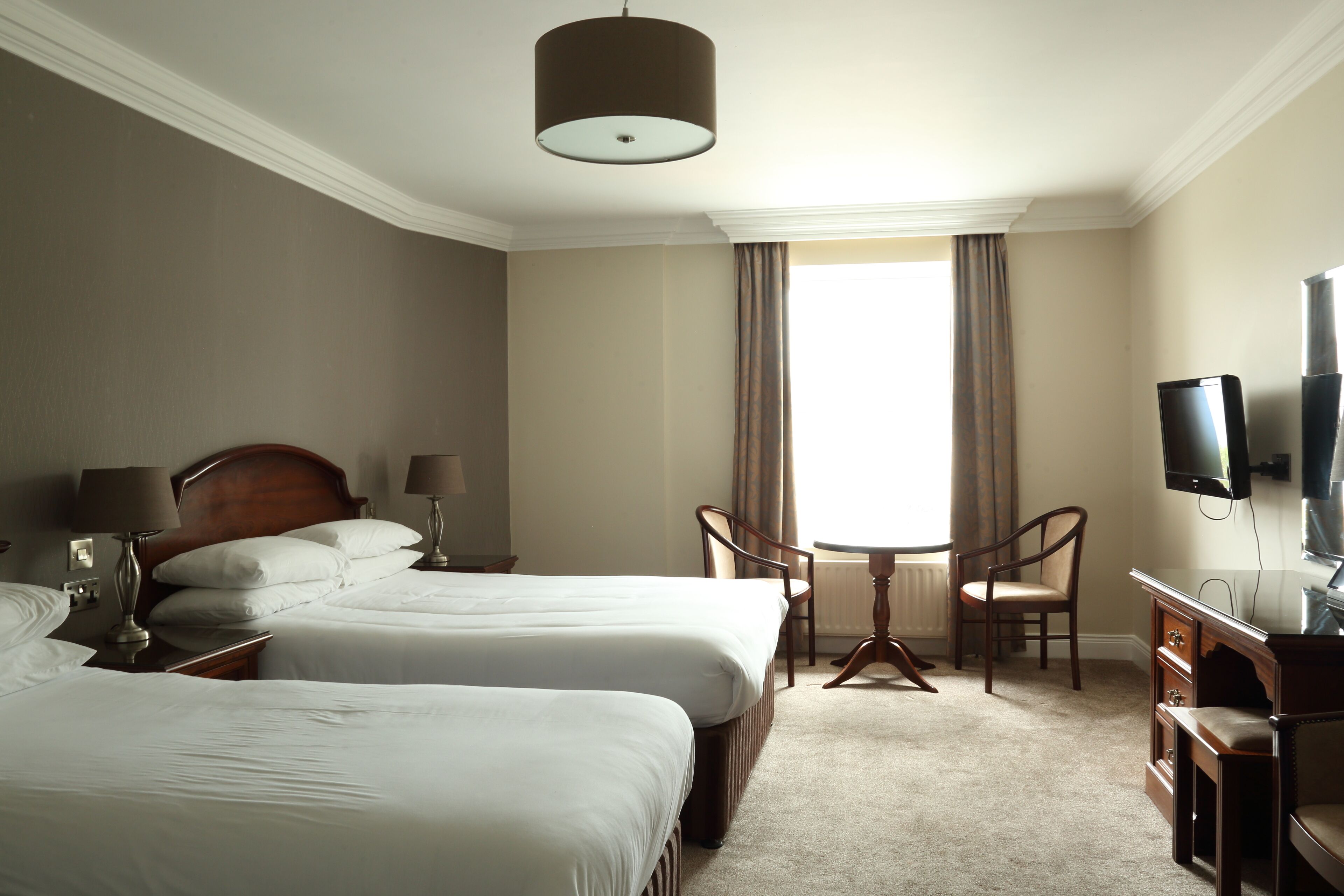 Une chambre d’hôtel avec deux lits, un bureau avec une chaise, une télévision et une fenêtre avec des rideaux.
