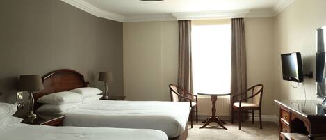 Une chambre d’hôtel avec deux lits, un bureau avec une chaise, une télévision et une fenêtre avec des rideaux.