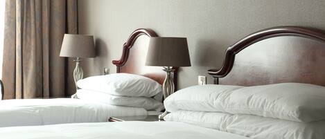 A hotel room with two beds, each with white linens and pillows, a wooden headboard, and two bedside lamps.