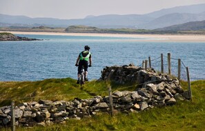 A coastal view with a cyclist on a path, a beach, and distant mountains. - The Abbey Hotel Donegal (Donegal)