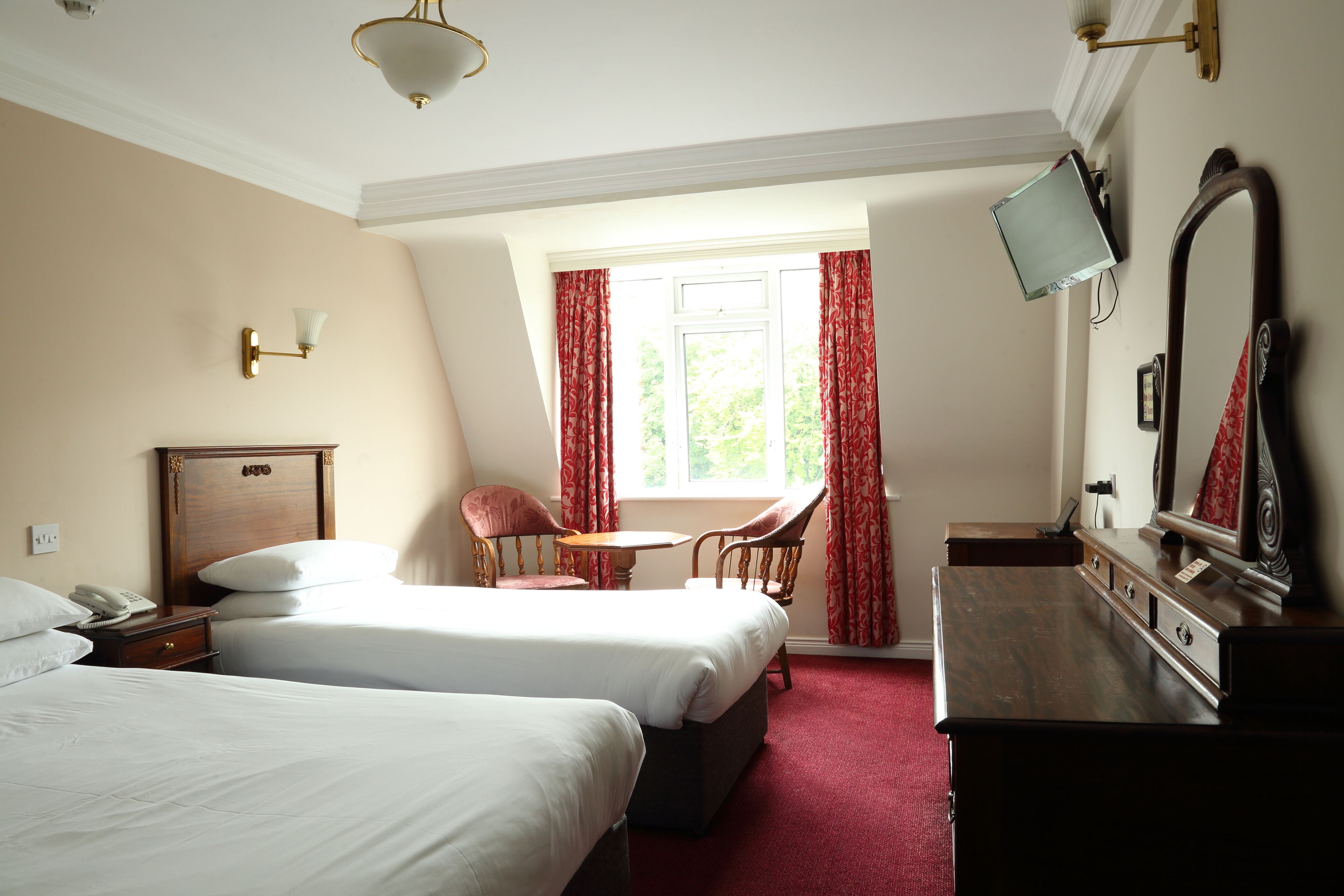 A hotel room with two beds, a desk, a chair, a TV, and a window with curtains.