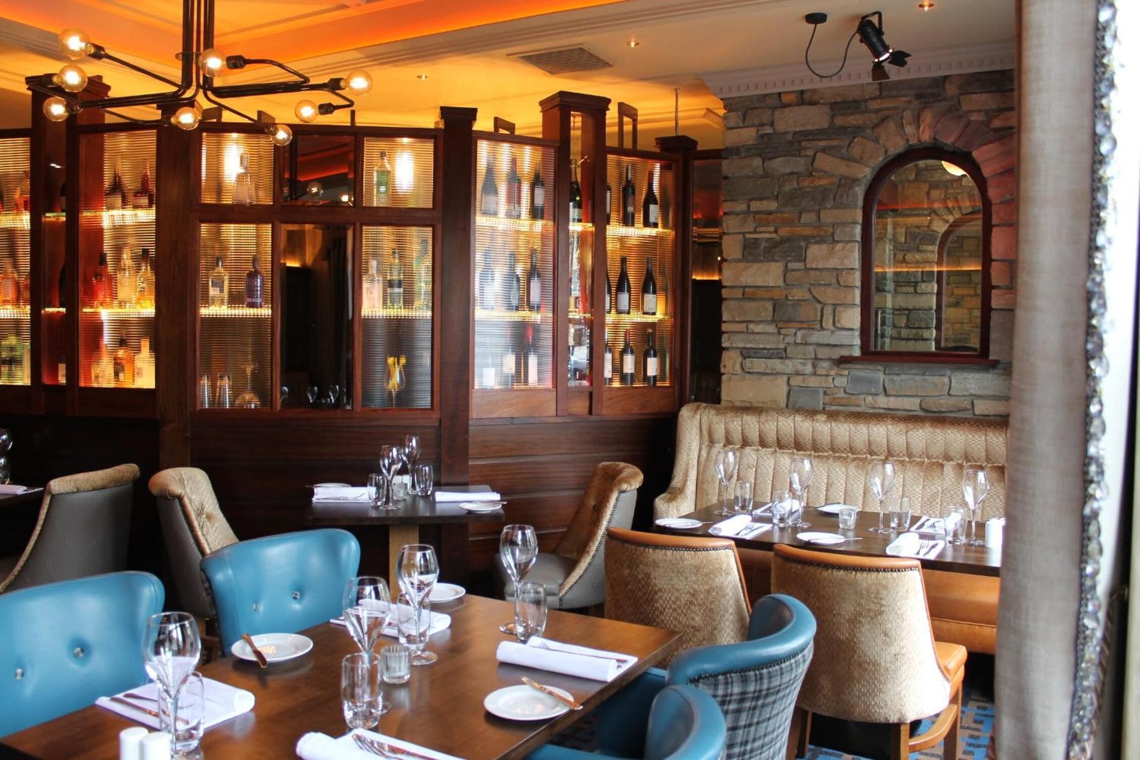 A restaurant with wooden paneled walls, stone accents, and blue upholstered chairs.
