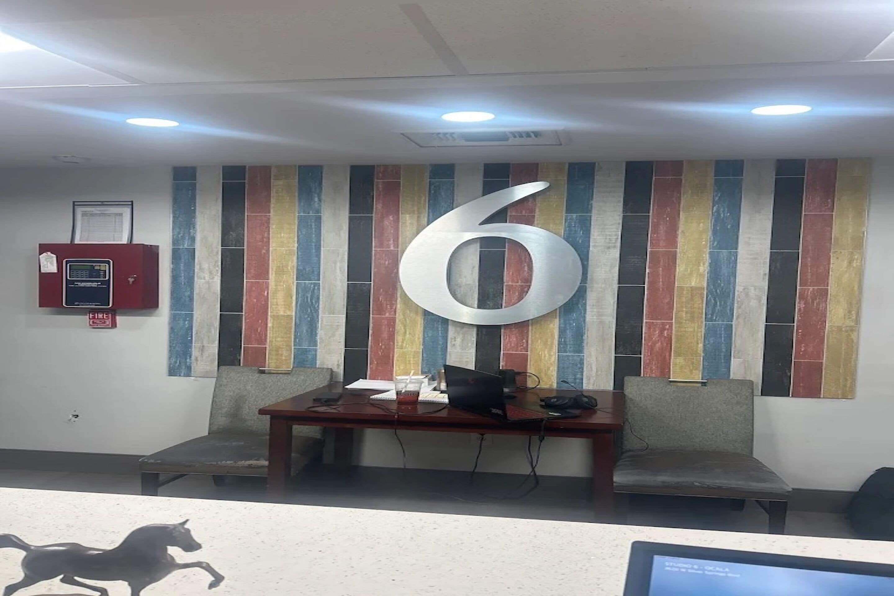 A reception area with a large number '6' on the wall, a fire alarm, and a desk with a computer and chair.