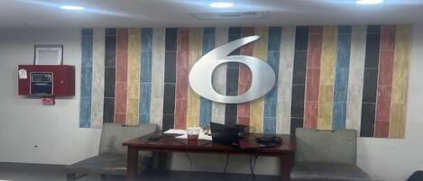 A reception area with a large number '6' on the wall, a fire alarm, and a desk with a computer and chair.