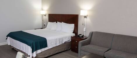 Habitación de hotel con una cama grande, lámparas de noche, mesita de noche, sofá y una silla.