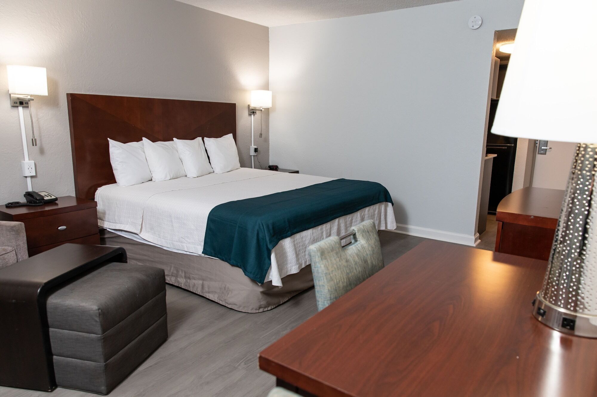 A hotel room with a bed, bedside tables, a desk, a chair, and a lamp.