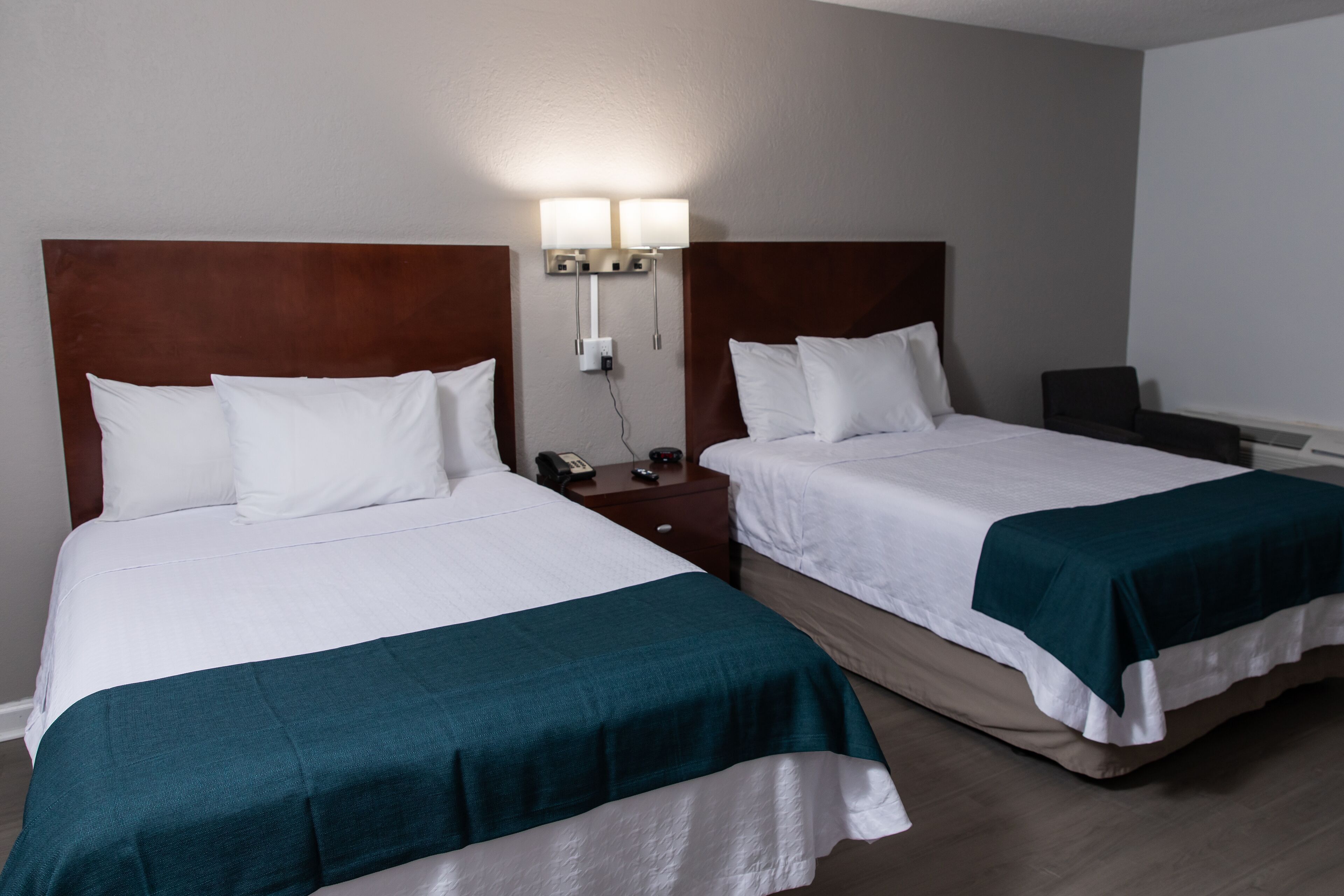 Two single beds with white linens and teal bedspreads, a wooden headboard, a bedside table with a phone, and a wall-mounted light fixture.