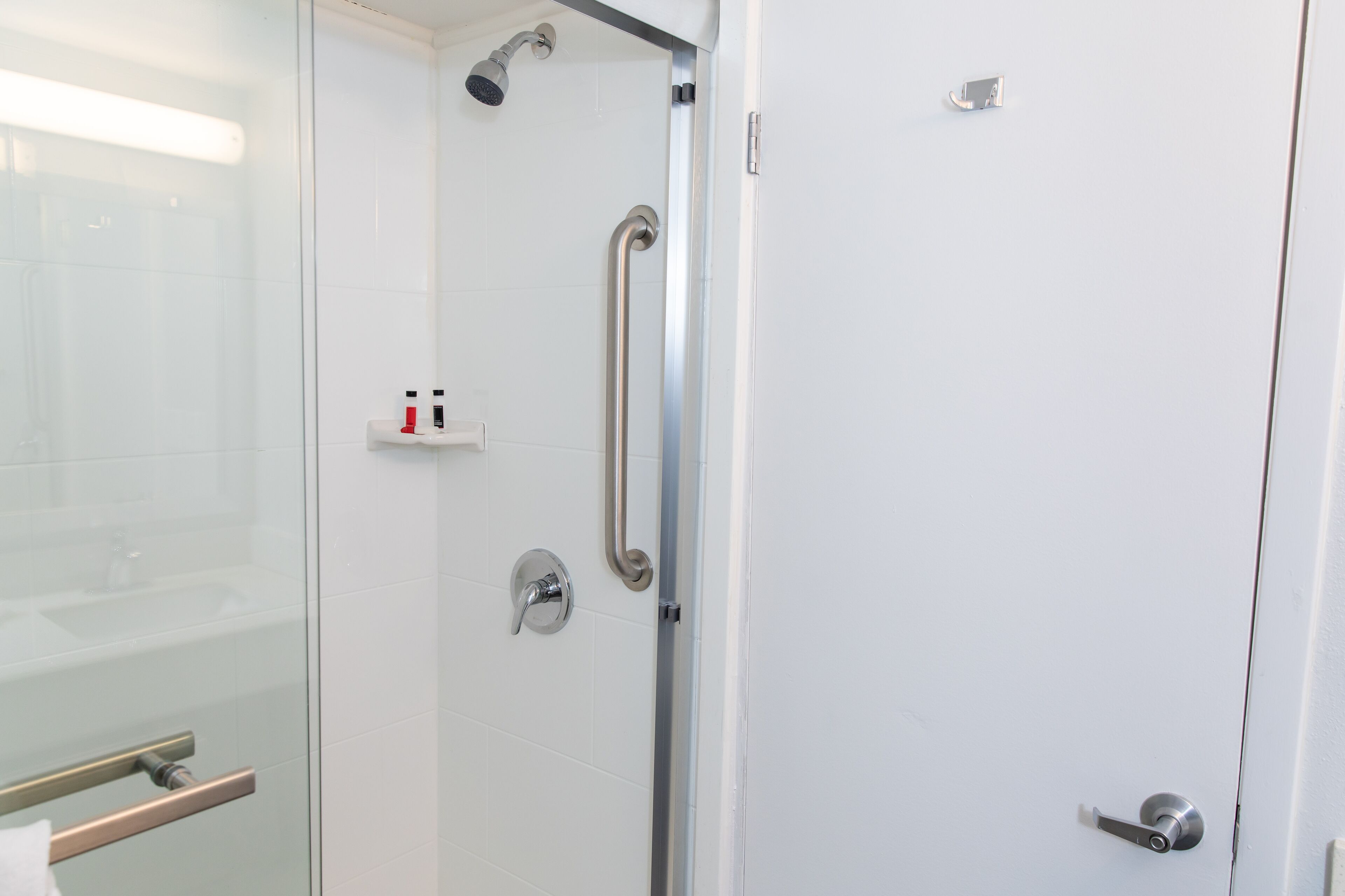 A modern bathroom with a glass shower enclosure, a handrail, and a toilet with a bidet attachment.