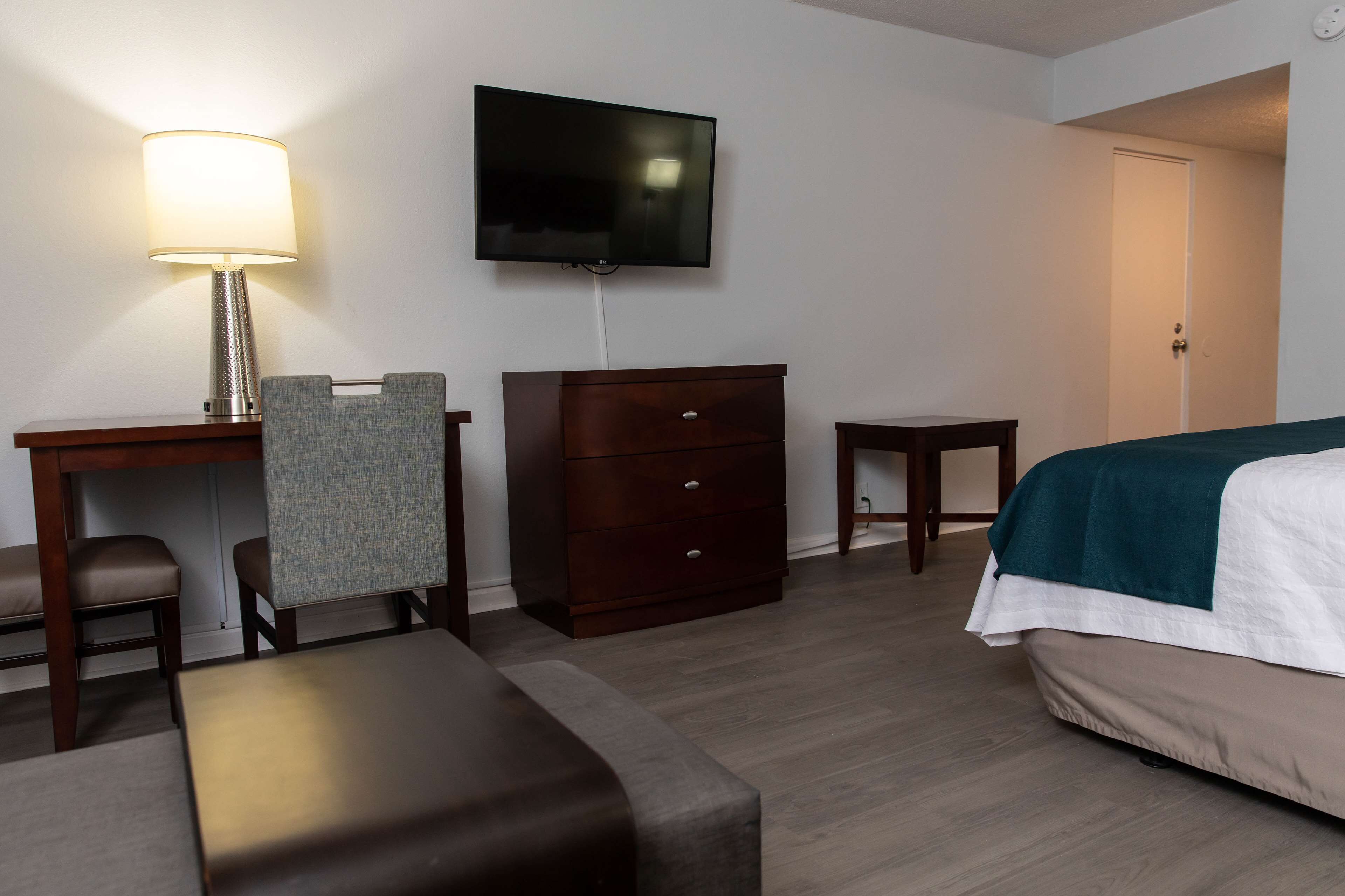 Une chambre d’hôtel comprenant un lit, un bureau avec une lampe, une télévision, une commode et une petite table.
