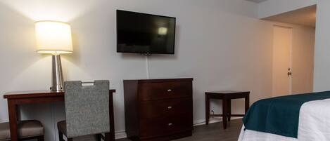 Une chambre d’hôtel comprenant un lit, un bureau avec une lampe, une télévision, une commode et une petite table.