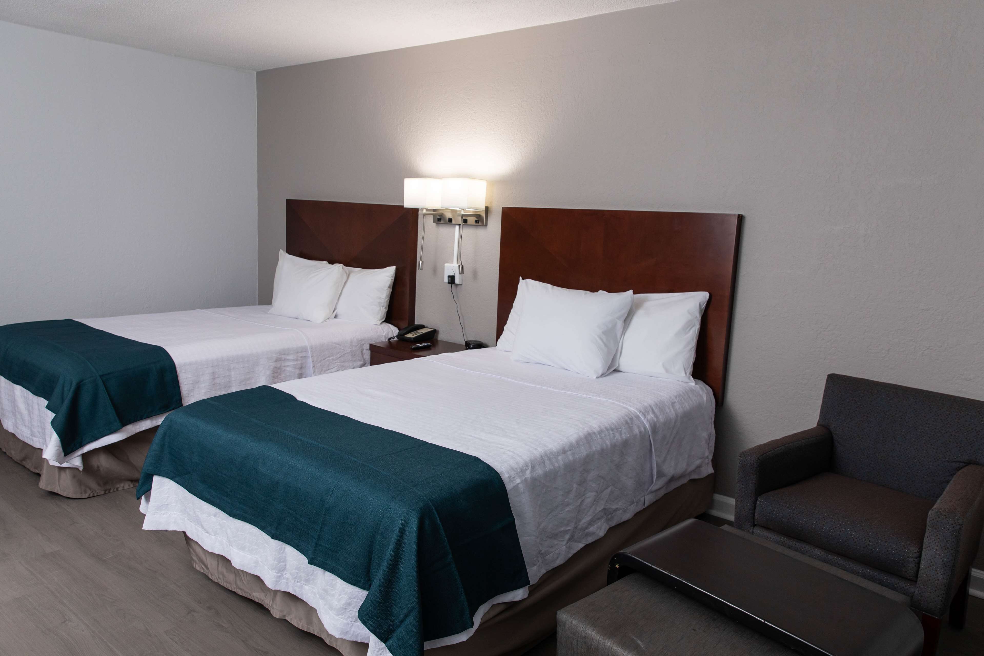 A hotel room with two single beds, a nightstand with a lamp, a chair, and a bench.