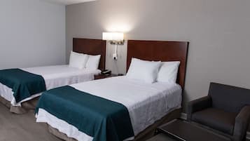 Una habitación de hotel con dos camas individuales, una mesita de noche con lámpara, una silla y un banco.