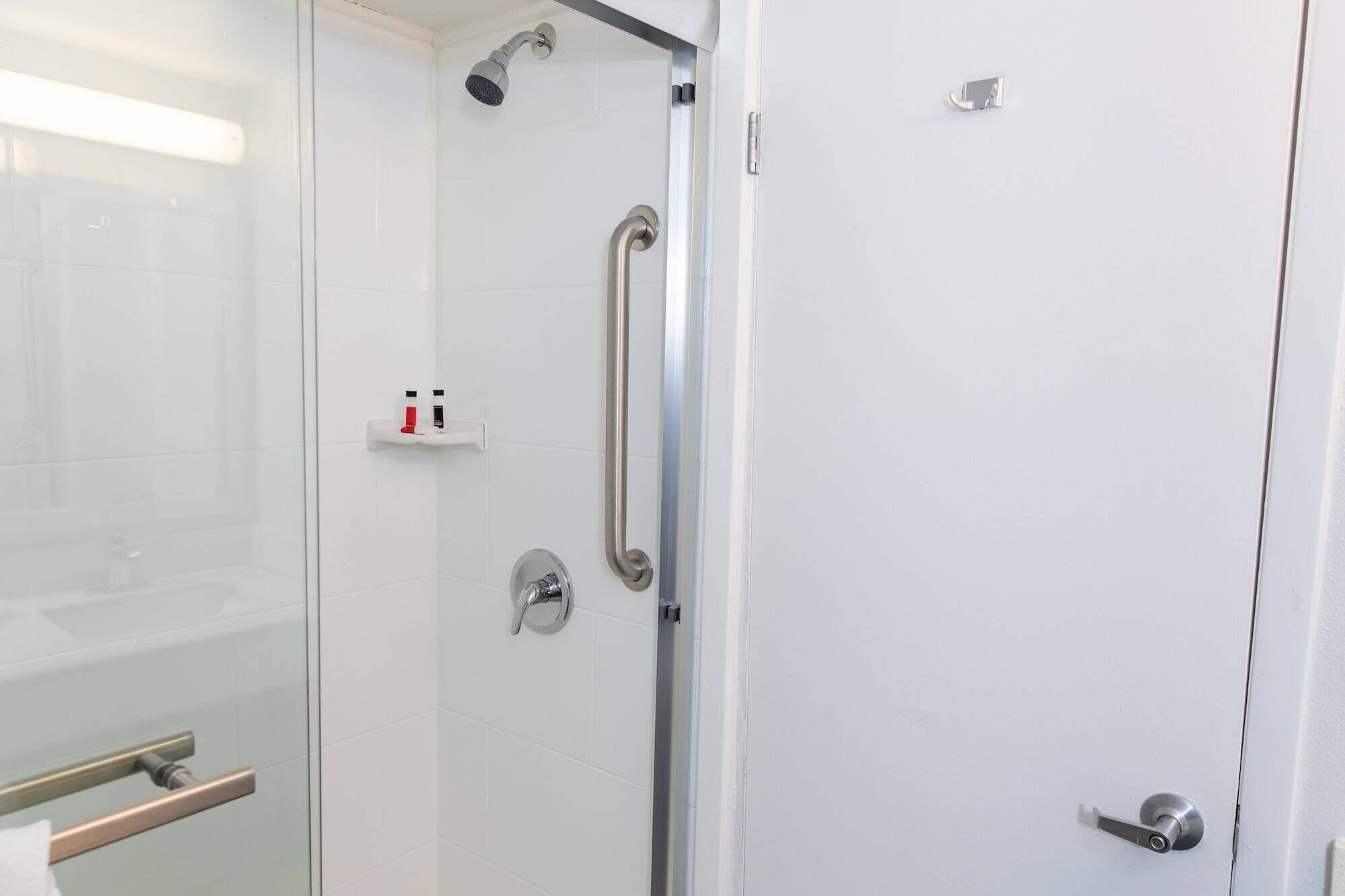 A modern bathroom with a glass shower enclosure, a handheld showerhead, a handheld shower control, and a towel rack.