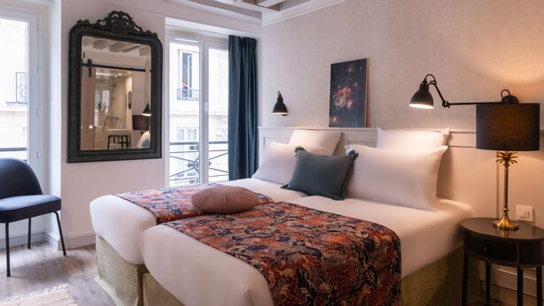 Habitación de hotel con cama, una silla, escritorio, espejo y ventana con cortinas.