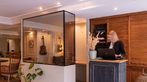 Mostrador de recepción con una computadora portátil, una planta en maceta y una guitarra al fondo.