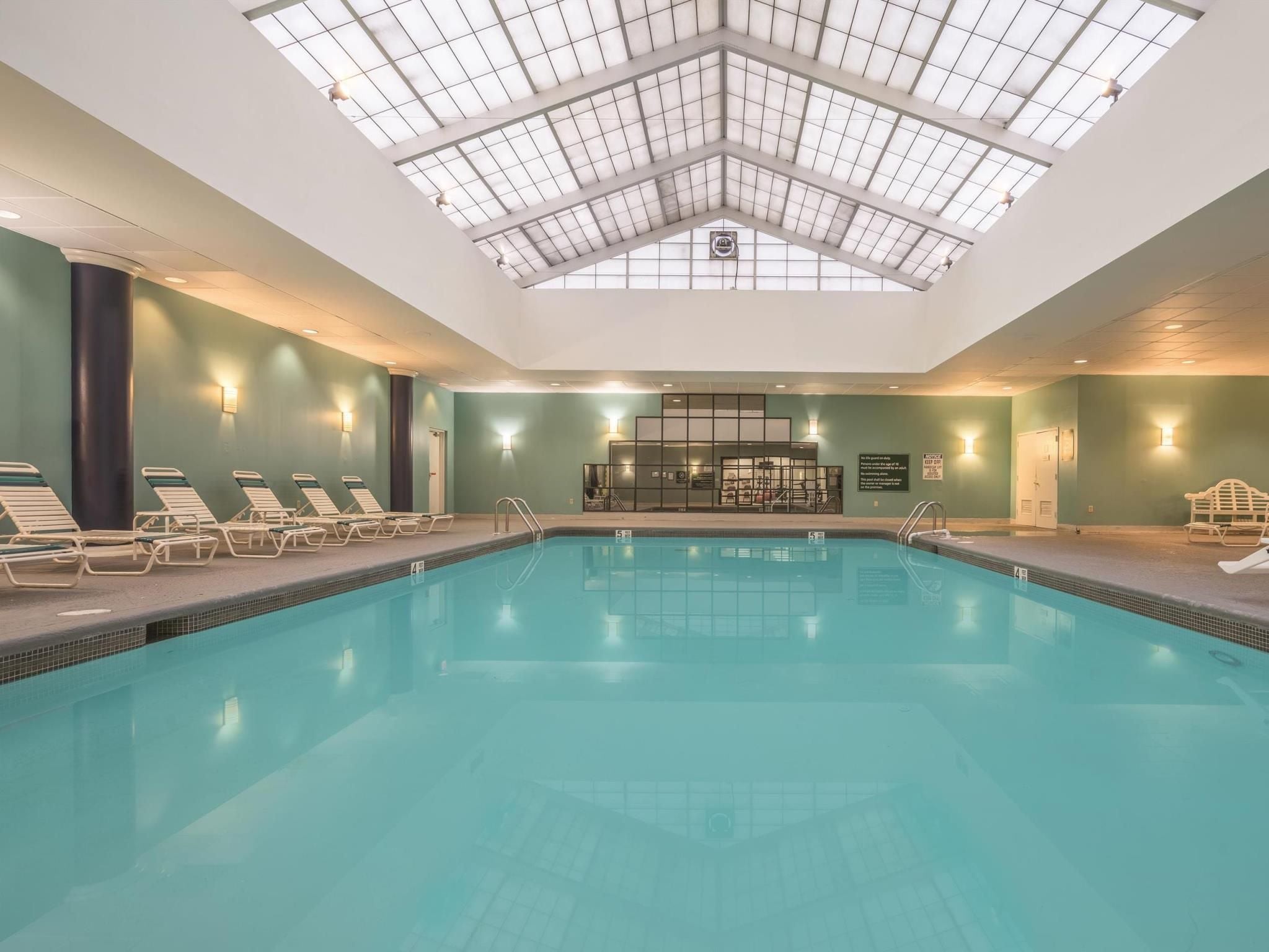 An indoor swimming pool with clear blue water, surrounded by lounge chairs and a glass ceiling.