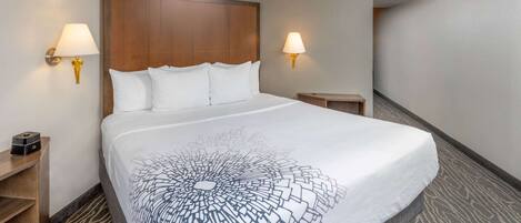 A hotel room with a large bed, two bedside lamps, a wooden headboard, and a small nightstand with a lamp.