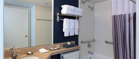 Un baño con lavamanos, inodoro y bañera. Hay toallas y una caja de pañuelos en el mostrador.
