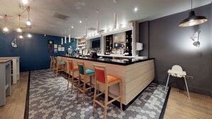 A modern bar area with a black countertop, wooden bar stools, and a hexagonal patterned floor. - Holiday Inn Runcorn by IHG (Runcorn)