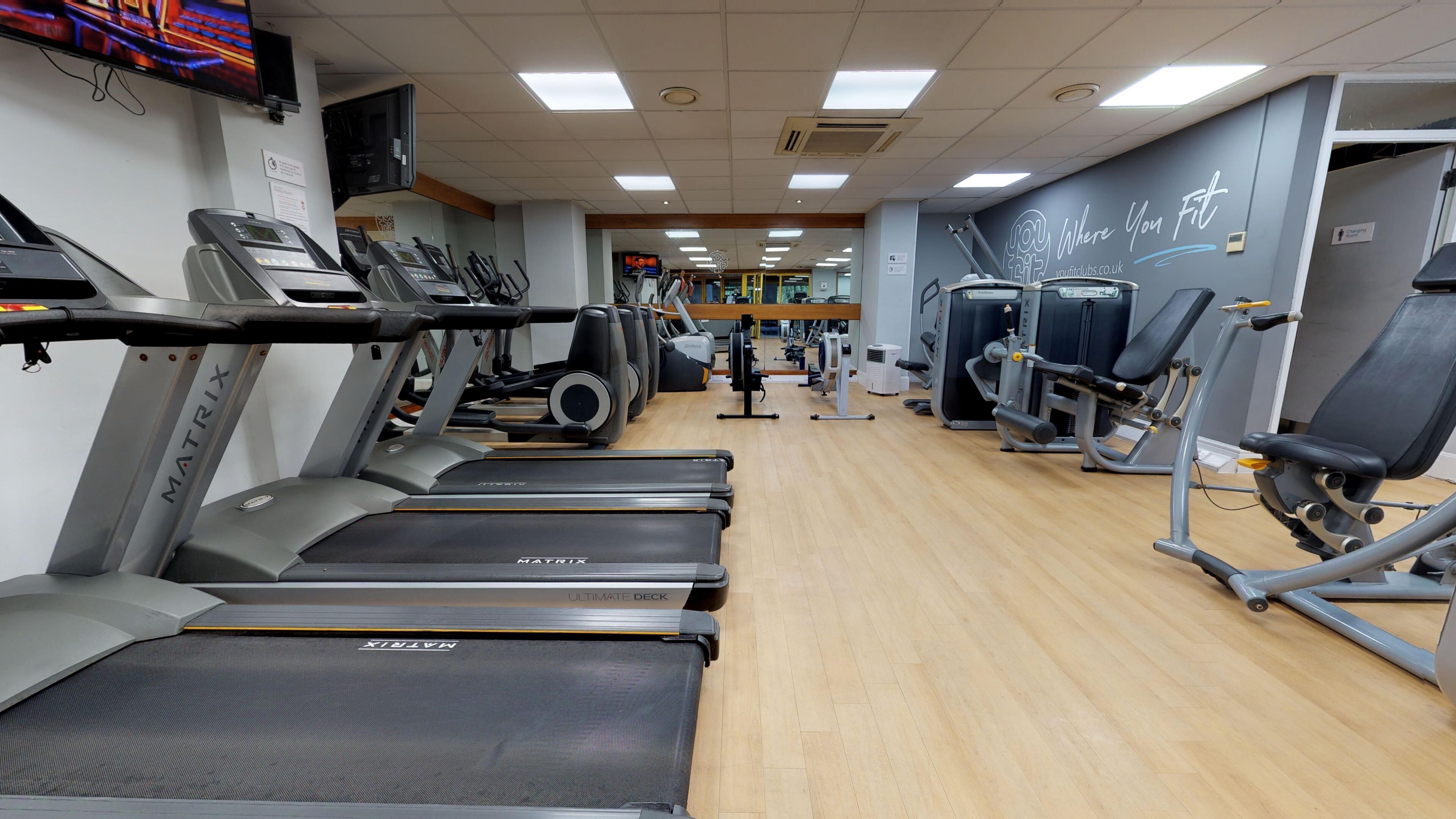 A gym with treadmills, weight machines, and a mirrored wall.