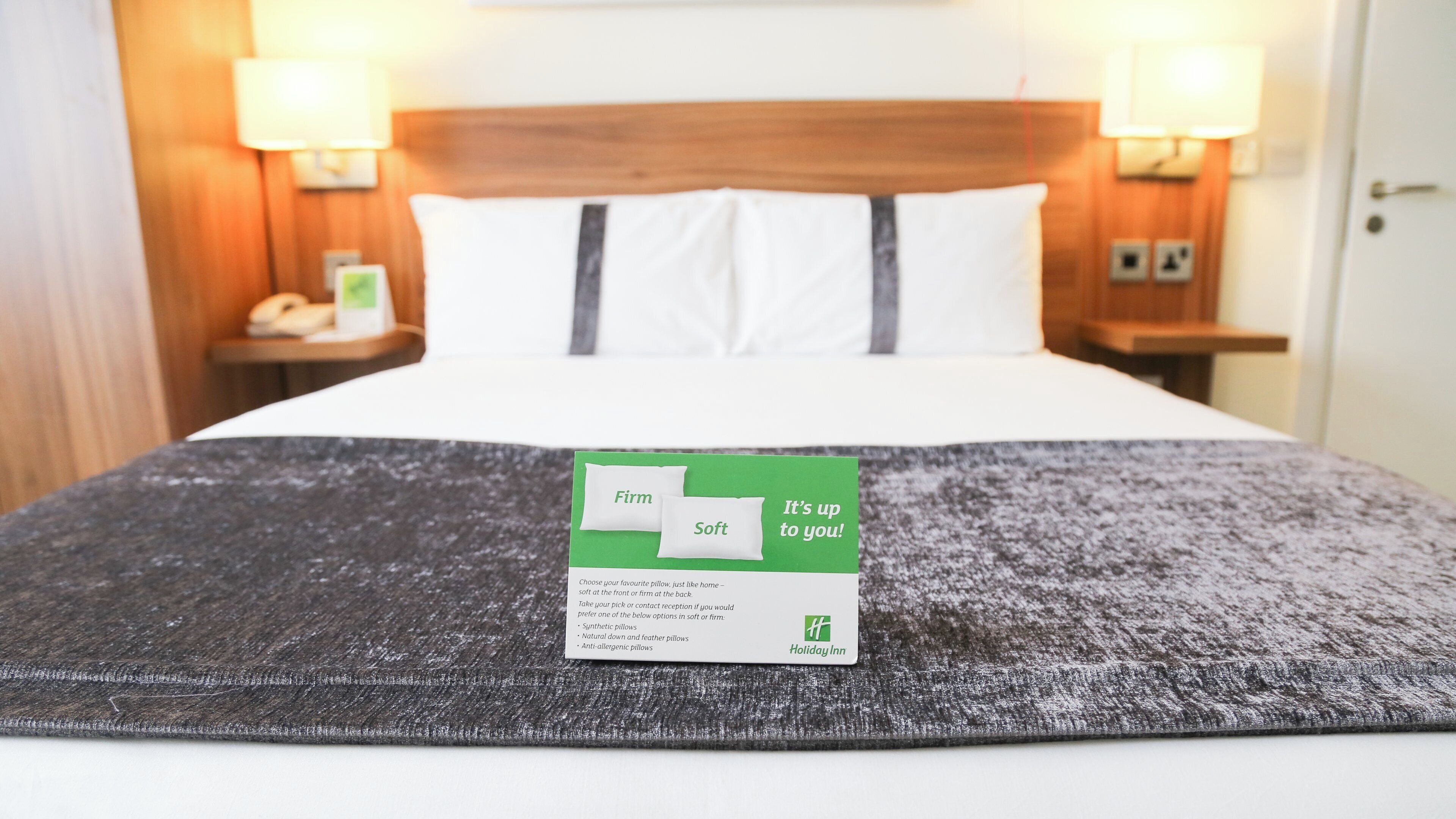 A hotel room with a bed, pillows, a blanket, and a card on the bed.