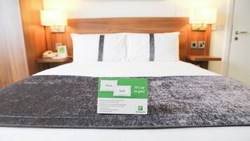 A hotel room with a bed, pillows, a blanket, and a card on the bed.